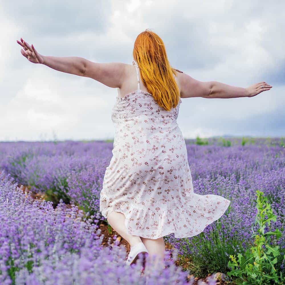 Young woman with long red hair wearing a floral dress running through lavender field